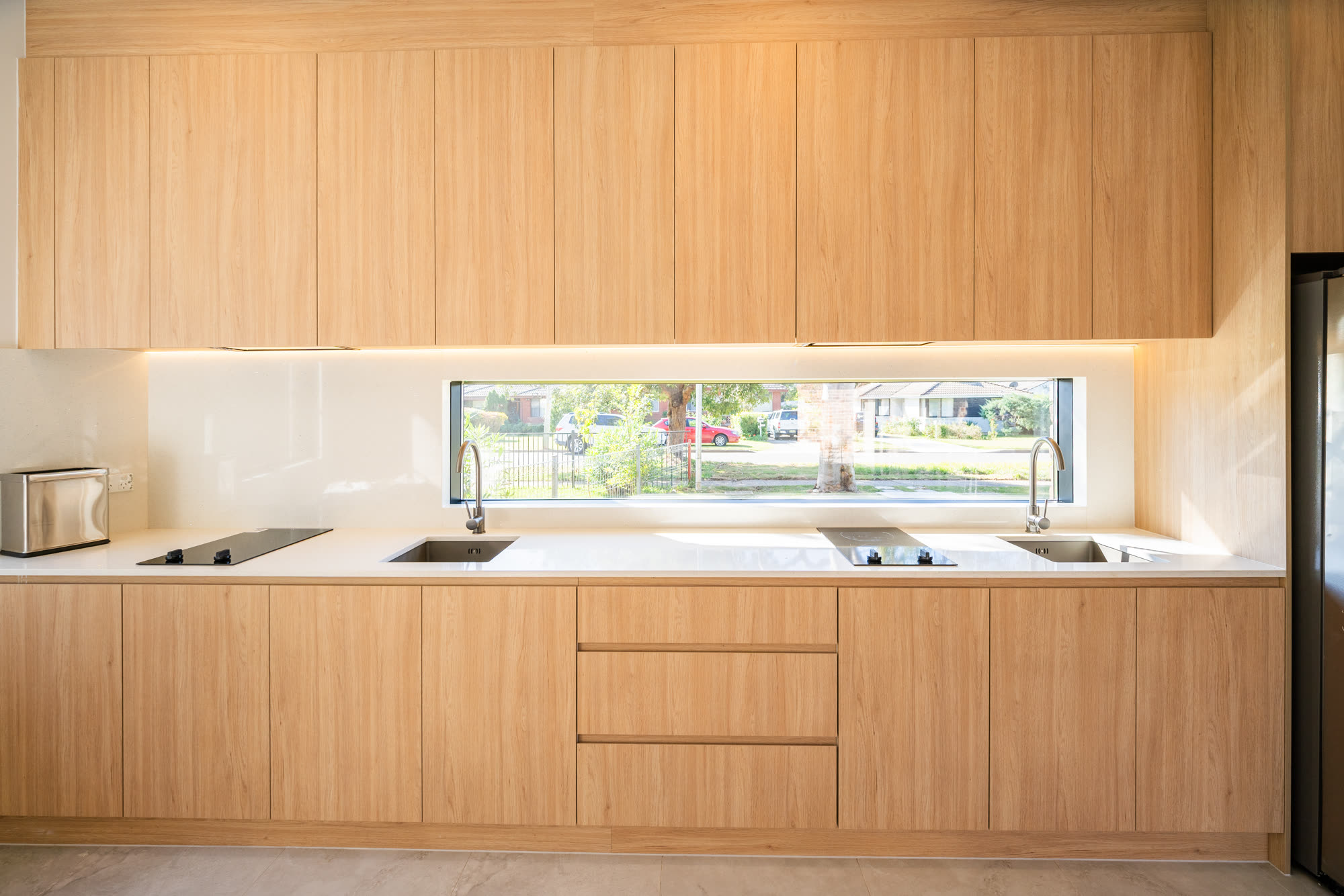 Shared kitchen in a Western Sydney co-living home, with two cooktops, two sinks, full-height timber joinery and a long window above the benchtop